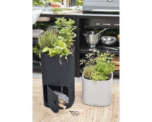 Två blomlådor med örter på en matta framför ett utekök.