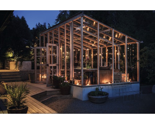 Växthus med träram, glasväggar och belysning i trädgården på natten.