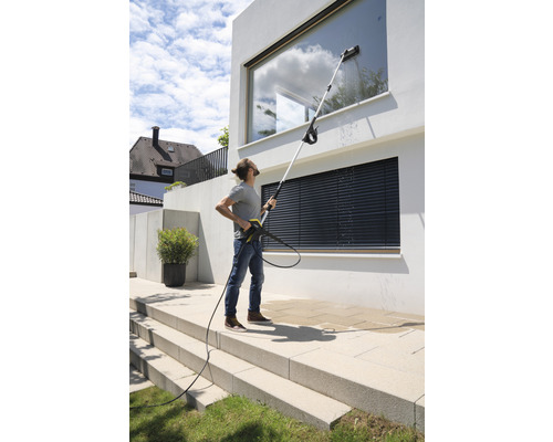 En person rengör fönster på ett modernt hus med en högtryckstvätt och en teleskopisk lans.