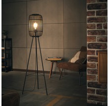 Golvlampa med metallskärm och stativ med tre ben i vardagsrummet.