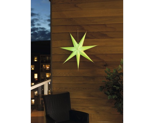 Dekorativ pappersstjärna på en trävägg, med en stol och en växt i bilden.