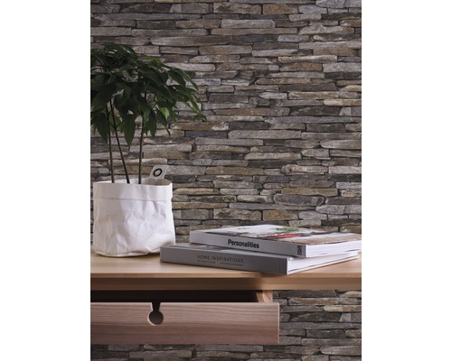 Väggbeklädnad med stenutseende, växt i papperspåse och böcker på ett träskrivbord
