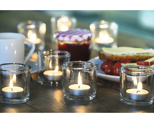 Bordsdekoration med värmeljus i glas, en burk marmelad och en smörgås