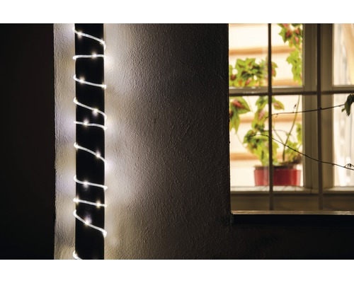 Dekorativ ljusslinga lindad runt en stolpe, krukväxt synlig i fönstret.