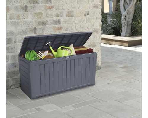 Öppen trädgårdsbox med trädgårdsredskap och sittdynor framför en vägg