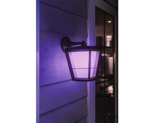 En sexkantig utomhusvägglampa med violett ljus på en husvägg.