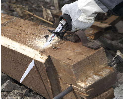 Hand med skyddshandske sågar en träbjälke med en tigersåg