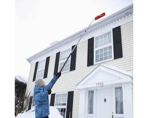 Person tar bort snö från ett hustak med en takskyffel.