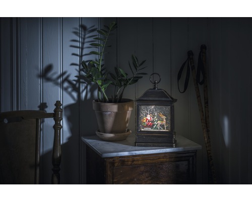 Dekorativ snöglobslykta med jultomte och ren på ett bord