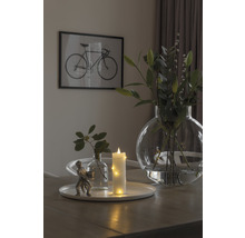 Dekorativt arrangemang med vas, ljus och figur på ett bord med en cykelbild i bakgrunden.