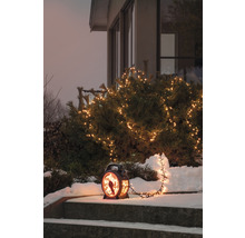 Dekorativ utomhuslampa med ljusslinga och fågelmotiv på en snöig trappa.