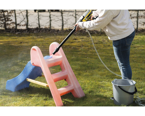 En person rengör en barnrutschkana med en högtryckstvätt i trädgården.
