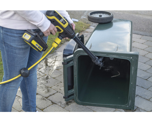 En person rengör en soptunna med en sladdlös högtryckstvätt.