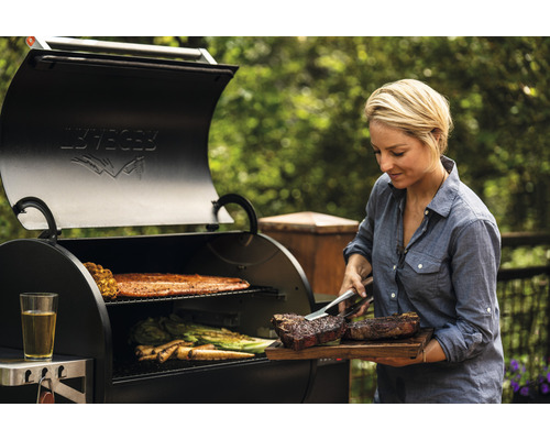 Kvinna grillar biffar, grönsaker och fisk på en Traeger grill utomhus