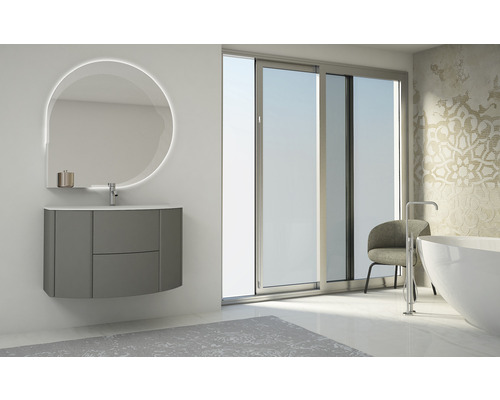 Badrum med handfat, upplyst spegel och badkar framför ett fönster