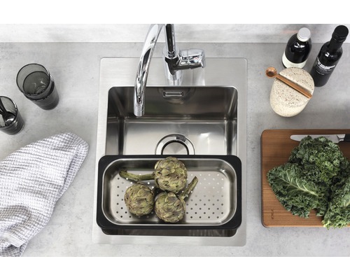 Rostfri diskho med droppbricka, kran, glas, kökshandduk, kryddor och grönsaker på en bänkskiva.