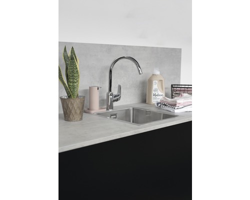 Tvättstuga med diskho, kran, tvåldispenser, tvättmedel och krukväxt på en bänkskiva