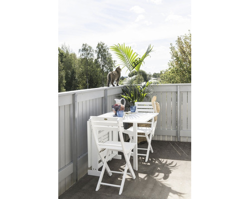 Balkongscen med vitt fällbord, stolar, dekorationer och en katt på balustraden