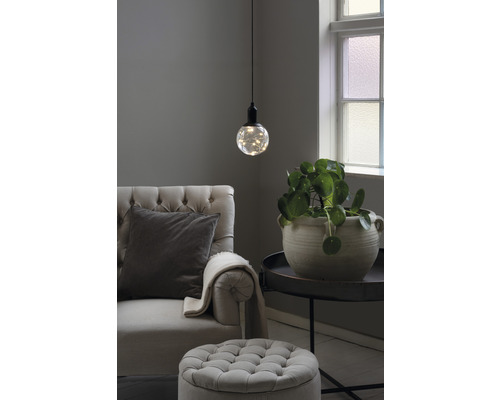 Vardagsrum med fåtölj, fotpall, bordslampa och krukväxt