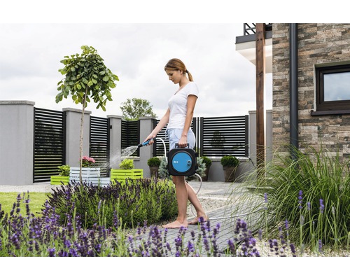 Kvinna vattnar växter med en slangbox i trädgården.