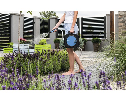 En kvinna vattnar växter i trädgården med en trädgårdsslangbox.