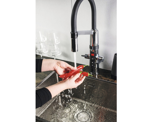 Händer tvättar röda chilipeppar under en kran i en diskho