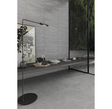 Modern interiör med grå vägg- och golvplattor, golvlampa och fönster med utsikt över trädgården.