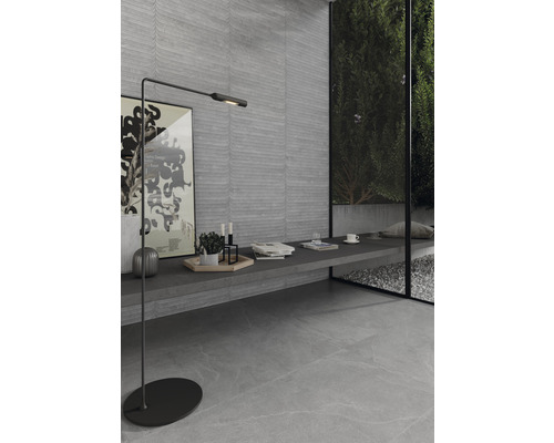 Modern interiör med grå vägg- och golvplattor, golvlampa och fönster med utsikt över trädgården.