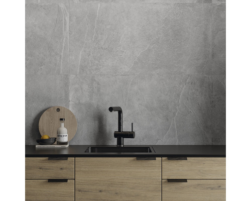 Köksscen med grå väggplattor, diskho och köksskåp i trä.