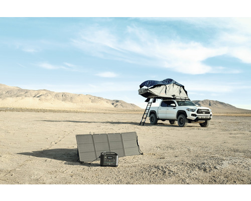 Campingutrustning med solpanel och bärbar kraftstation bredvid en pickup med taktält i öknen