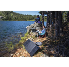 Scen vid sjön med portabel solpanel, kraftstation, bord och campingstolar för utomhusbruk.