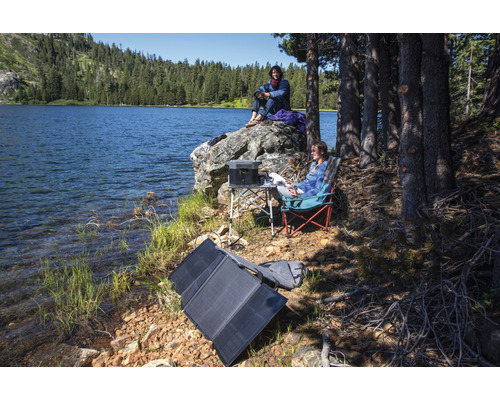 Scen vid sjön med portabel solpanel, kraftstation, bord och campingstolar för utomhusbruk.