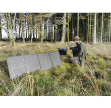 Man sitter på huk i skogen och använder en solcellsmodul för att ladda en generator