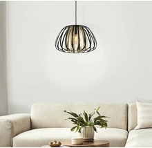 Hängande metallampa med öppen, bur-liknande design ovanför en soffa och ett soffbord med växt.