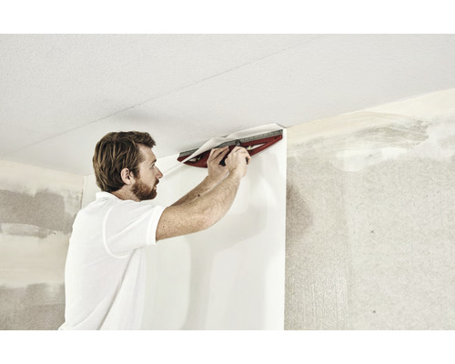 En man använder ett skärverktyg för att applicera tapeter på en vägg.
