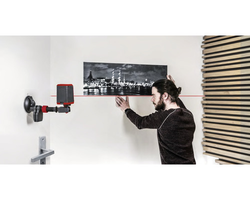 Man justerar en bild med ett laservattenpass på väggen.