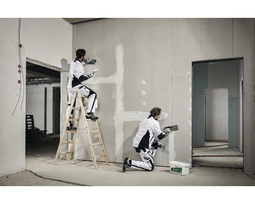 Två hantverkare spacklar en gipsskivevägg i ett råbygge.