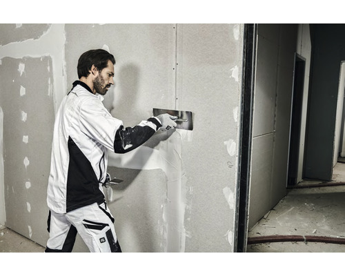En man spacklar en gipsskivevägg med en spackel.