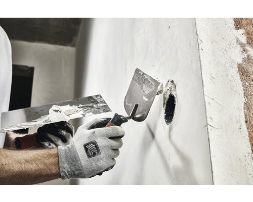 Hantverkare spacklar en vägg med två spacklar