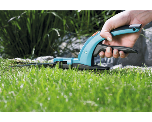 Hand som håller en grässax när du klipper gräs