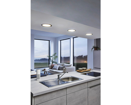 Ljust kök med infällda spotlights i taket, diskho och vardagsrum i bakgrunden.