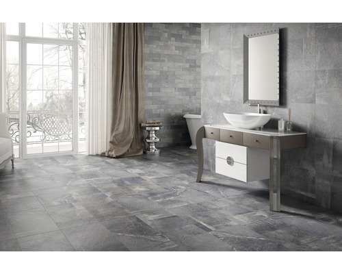 Modernt badrum med grå kakel på vägg och golv, tvättställsskåp, spegel och badkar.