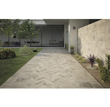 Uteplats med kaklad gång i fiskbensmönster, gräsmatta och planterade rabatter.