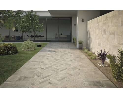 Uteplats med kaklad gång i fiskbensmönster, gräsmatta och planterade rabatter.