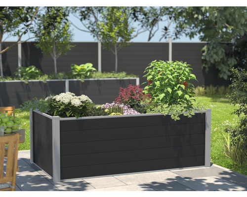 Hög pallkrage i plast med olika växter i en trädgård.