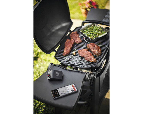 Grillscen med biffar, gröna grönsaker, grilltermometer och smartphone på en grill