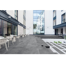 Utomhusområde med terrassplattor, bord och stolar framför byggnader