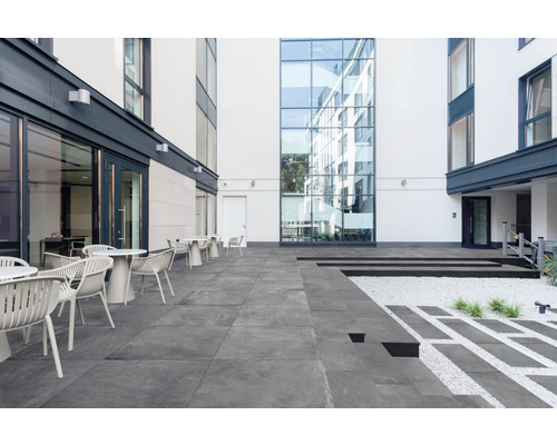 Utomhusområde med terrassplattor, bord och stolar framför byggnader