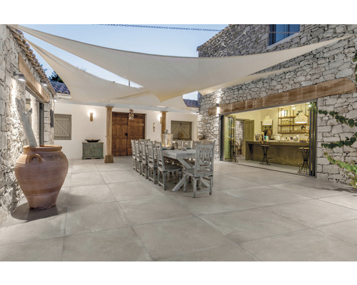 Uteplats med stengolv, matbord och solsegel