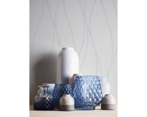 Dekorativa vaser av glas och keramik framför en mönstrad tapet